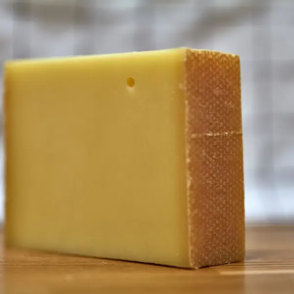 Ein Stück Bergkäse mit dunkler Rinde auf einem Holzbrett